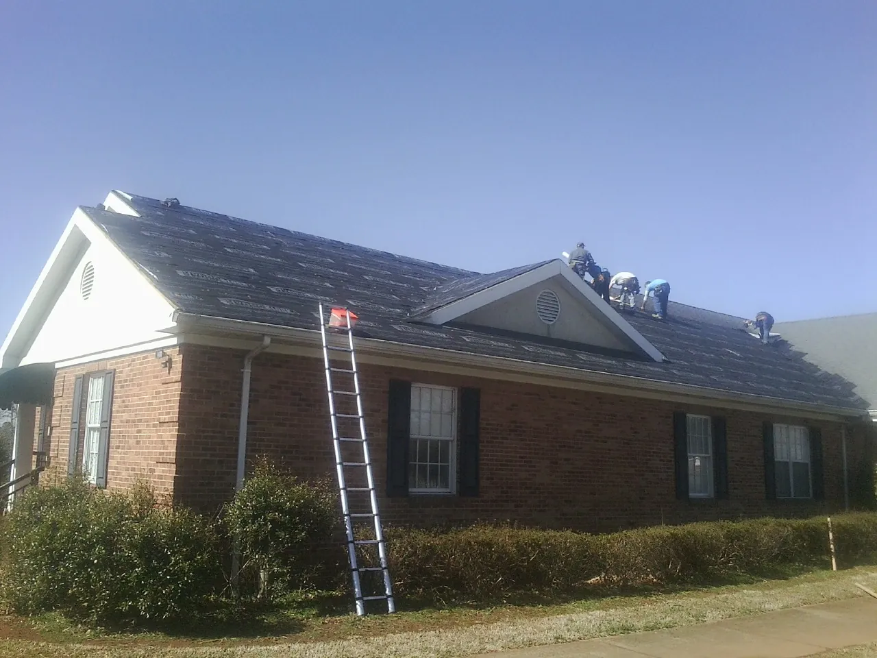 Crew tearing shingles off a brick ranch roof with a ladder set — Metal Roof Repair work by our crew in Von Ormy