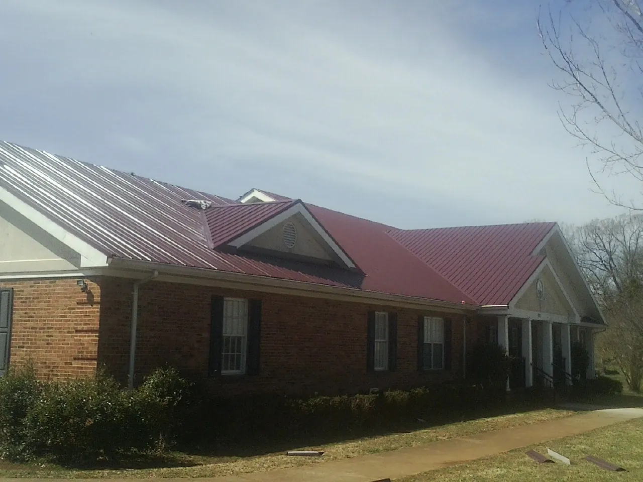 Red metal roof with gabled entries on a long brick building, from a Hail Damage Roof Repair job in Von Ormy