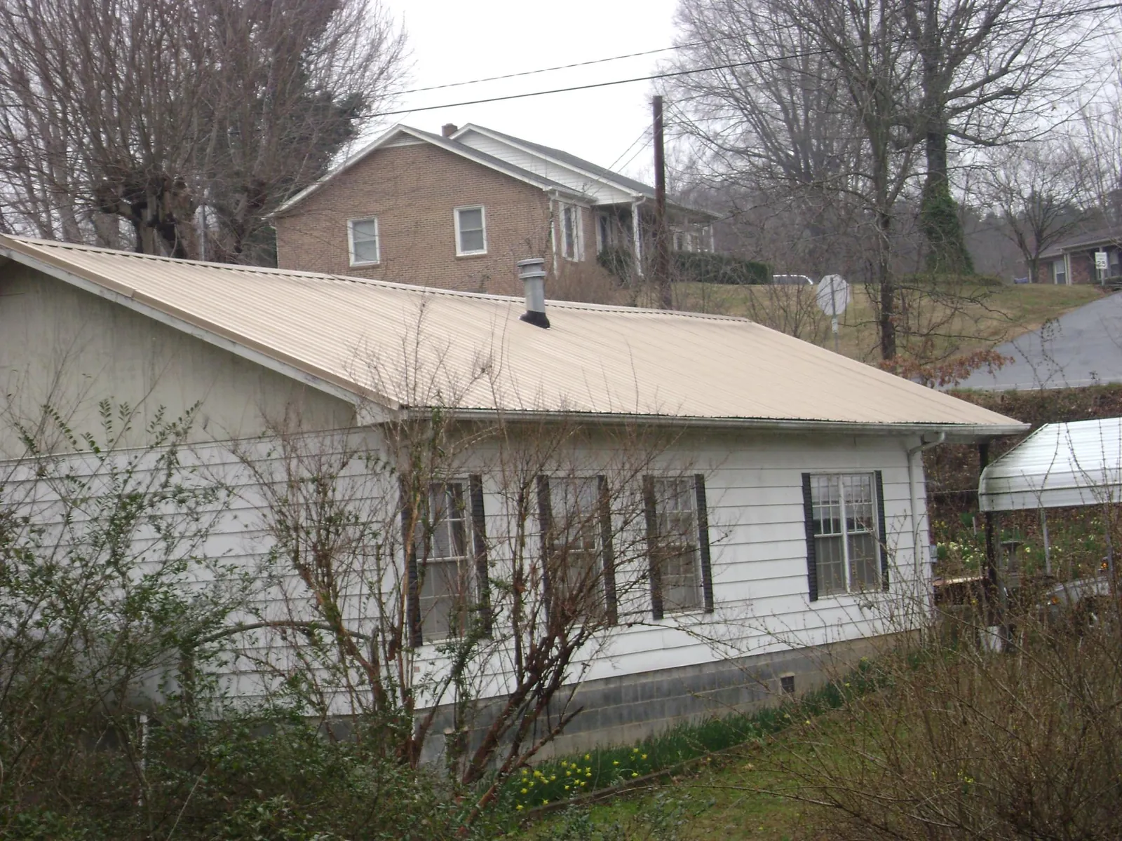 Tan metal roof on a white sided house set into a hillside — Commercial Roofing by Roofing Brothers in Von Ormy